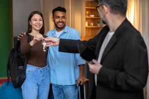 A man handing over the key to a couple, signifying a warm welcome and efficient short-term Airbnb management service for their stay